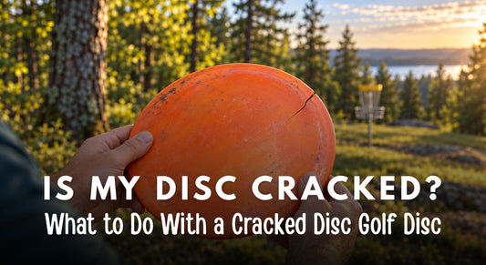 Hands holding a worn orange disc golf disc with a visible rim crack on a wooded course.