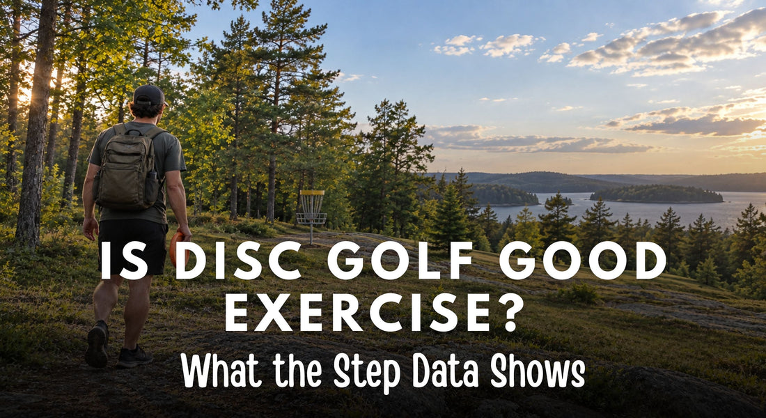 Disc golfer walking toward a basket on a wooded course overlooking a lake.