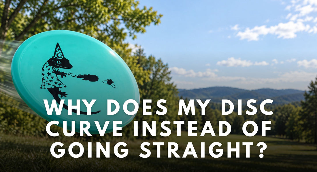 A turquoise disc with a black wizard-and-gecko stamp floats above a wooded disc golf fairway.